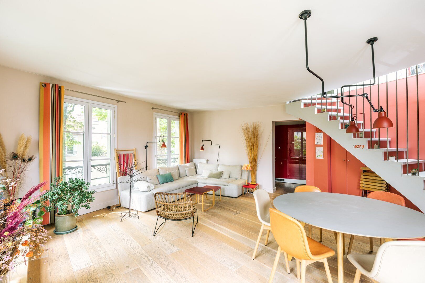 Una sala de estar moderna con un sofá blanco, una mesa de comedor con sillas y una escalera con detalles rojos.