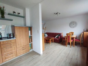 A compact living space with a kitchenette, a red sofa, a dining table with chairs, and a wall clock.