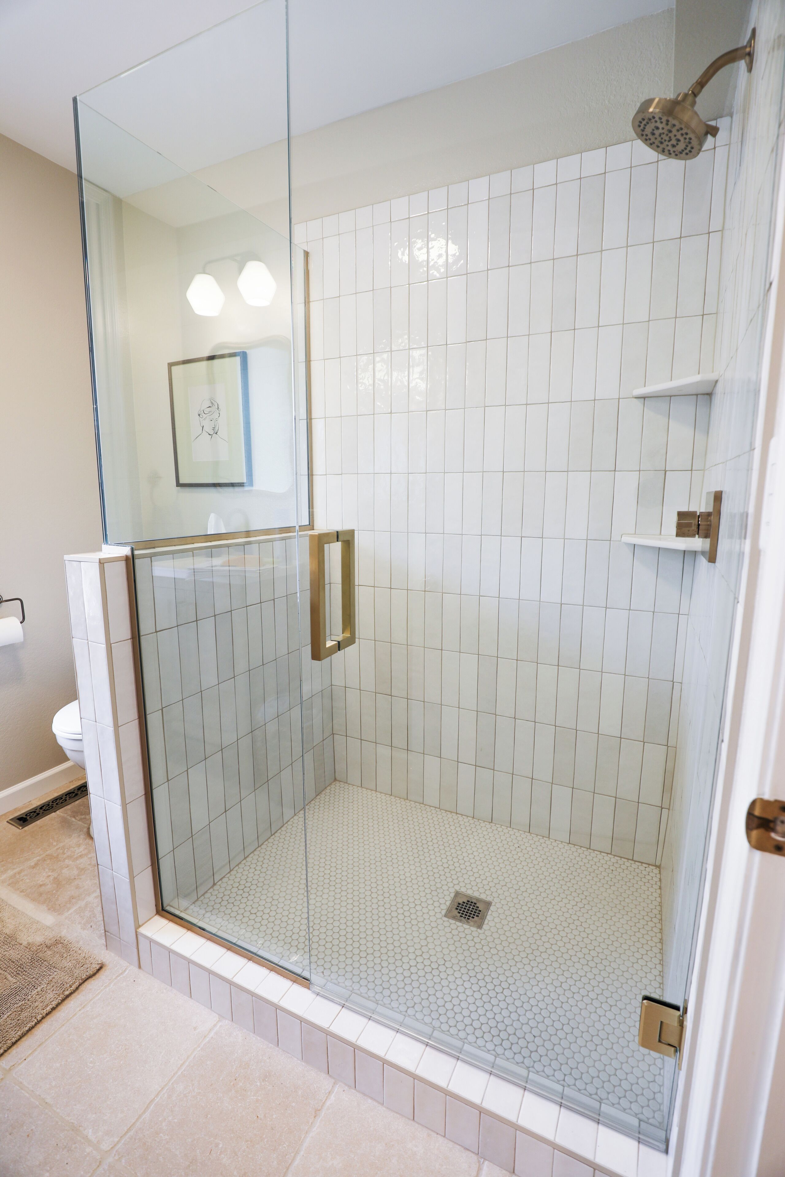 A glass-enclosed shower with a tiled floor and a handheld showerhead.