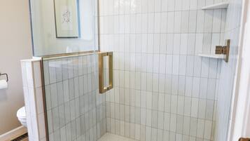 A glass-enclosed shower with a tiled floor and a handheld showerhead.