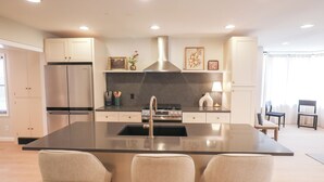 Une cuisine moderne dotée d’un îlot central, d’appareils électroménagers en acier inoxydable et d’un plan de travail noir.