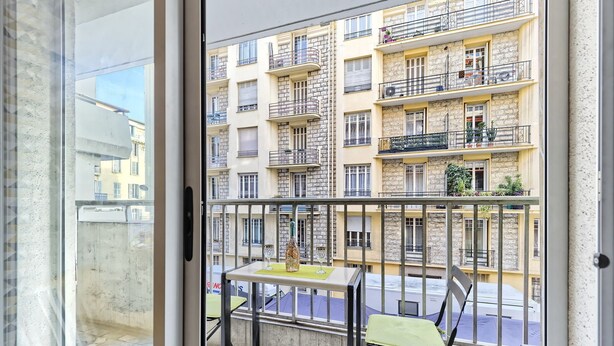 Un balcón con mesa y sillas, con vistas a un edificio de varios pisos con balcones.