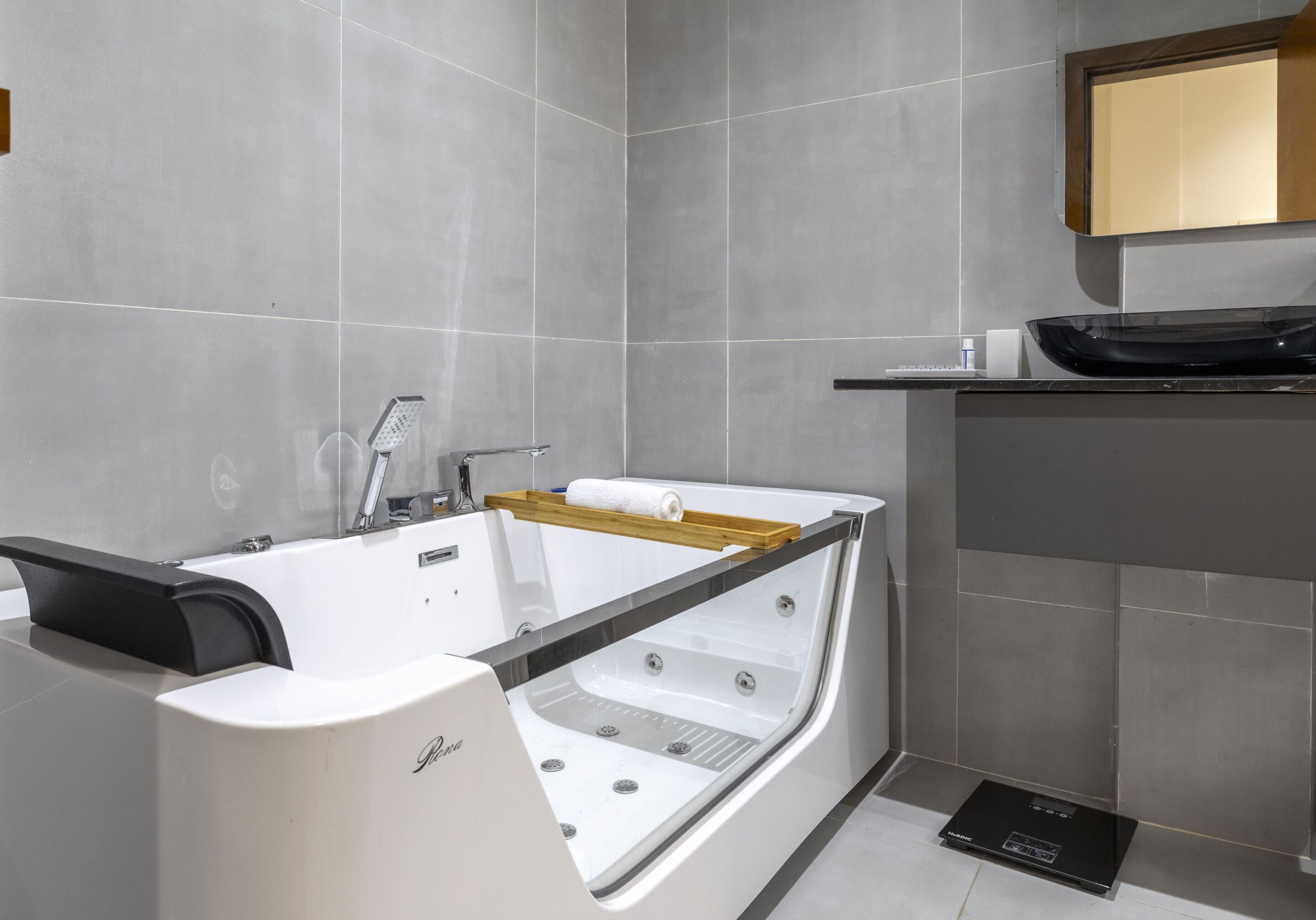 Un baño moderno con una bañera independiente, un estante de madera y una encimera negra.