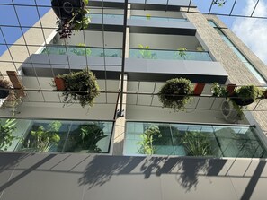 A modern building with multiple floors, large windows, and hanging planters with various plants.