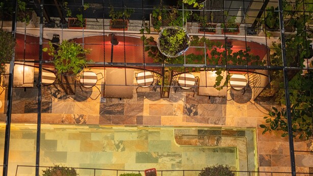 A pool area with tiled flooring, a seating area with striped cushions, and potted plants. - The Six Apparthotel (Abidjan)