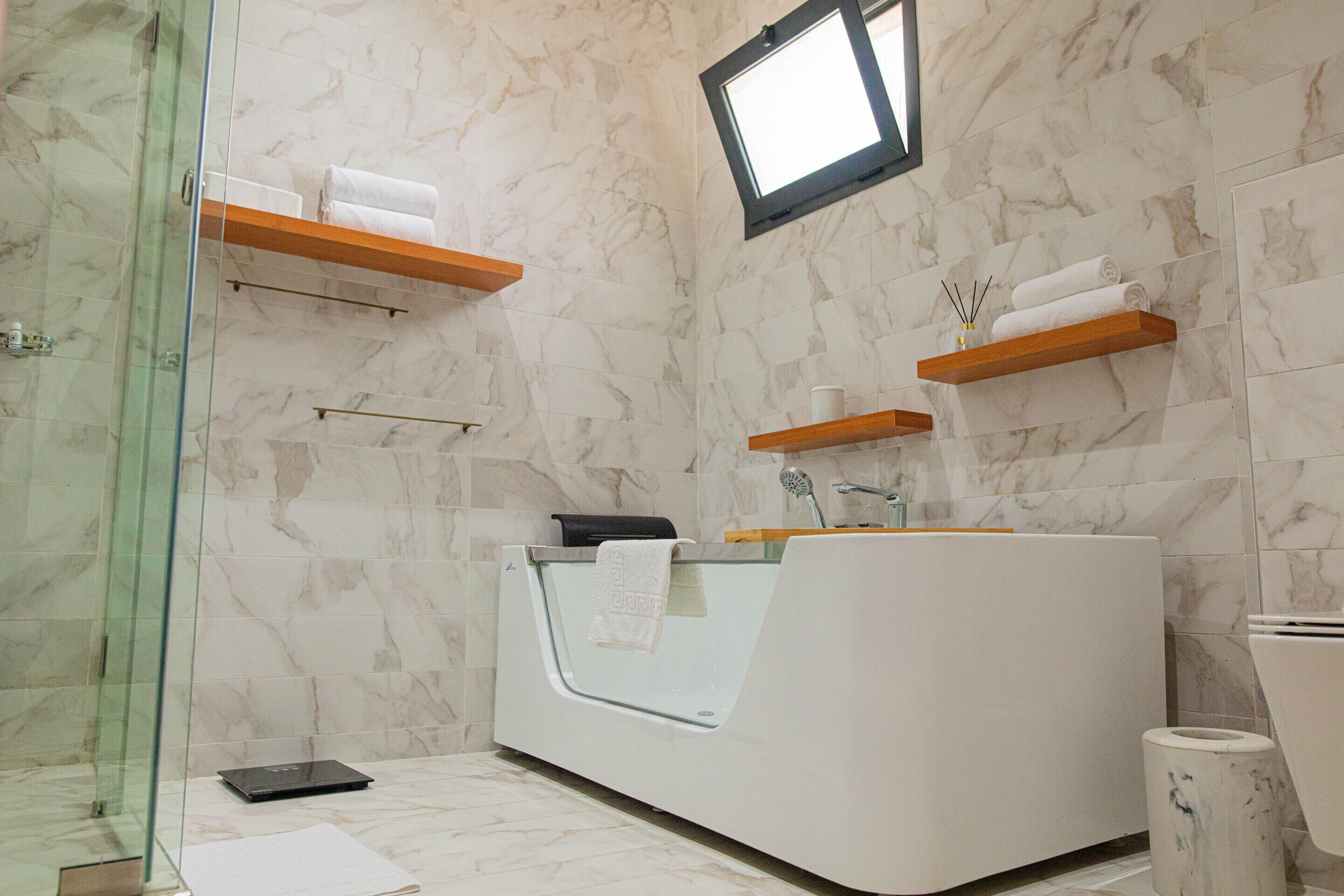 Un baño moderno con cabina de ducha de vidrio, una bañera blanca y paredes de mármol.