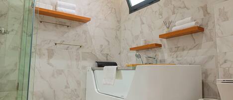 Un baño moderno con cabina de ducha de vidrio, una bañera blanca y paredes de mármol.