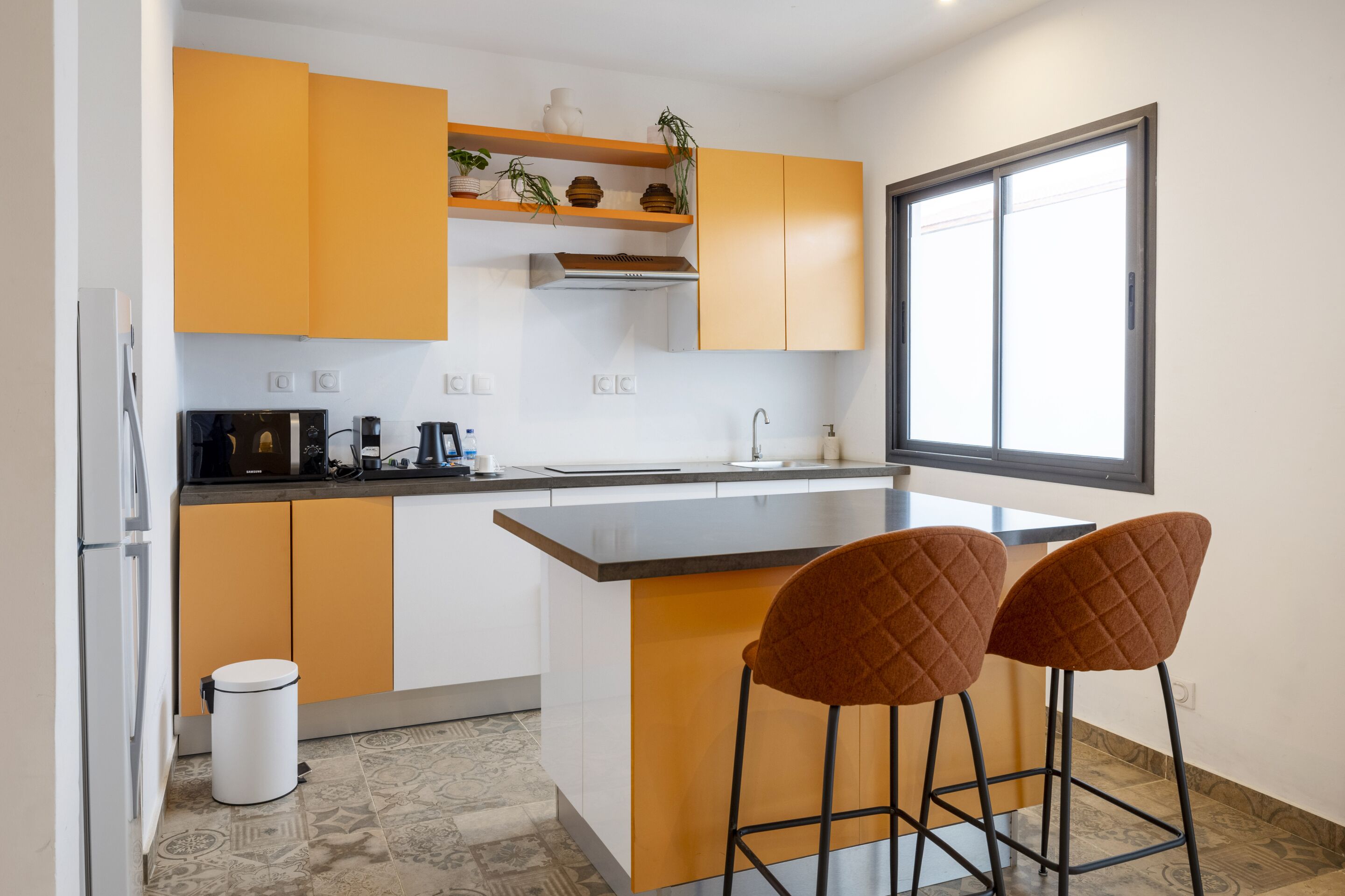 A modern kitchen with a central island, two bar stools, and a window providing natural light.