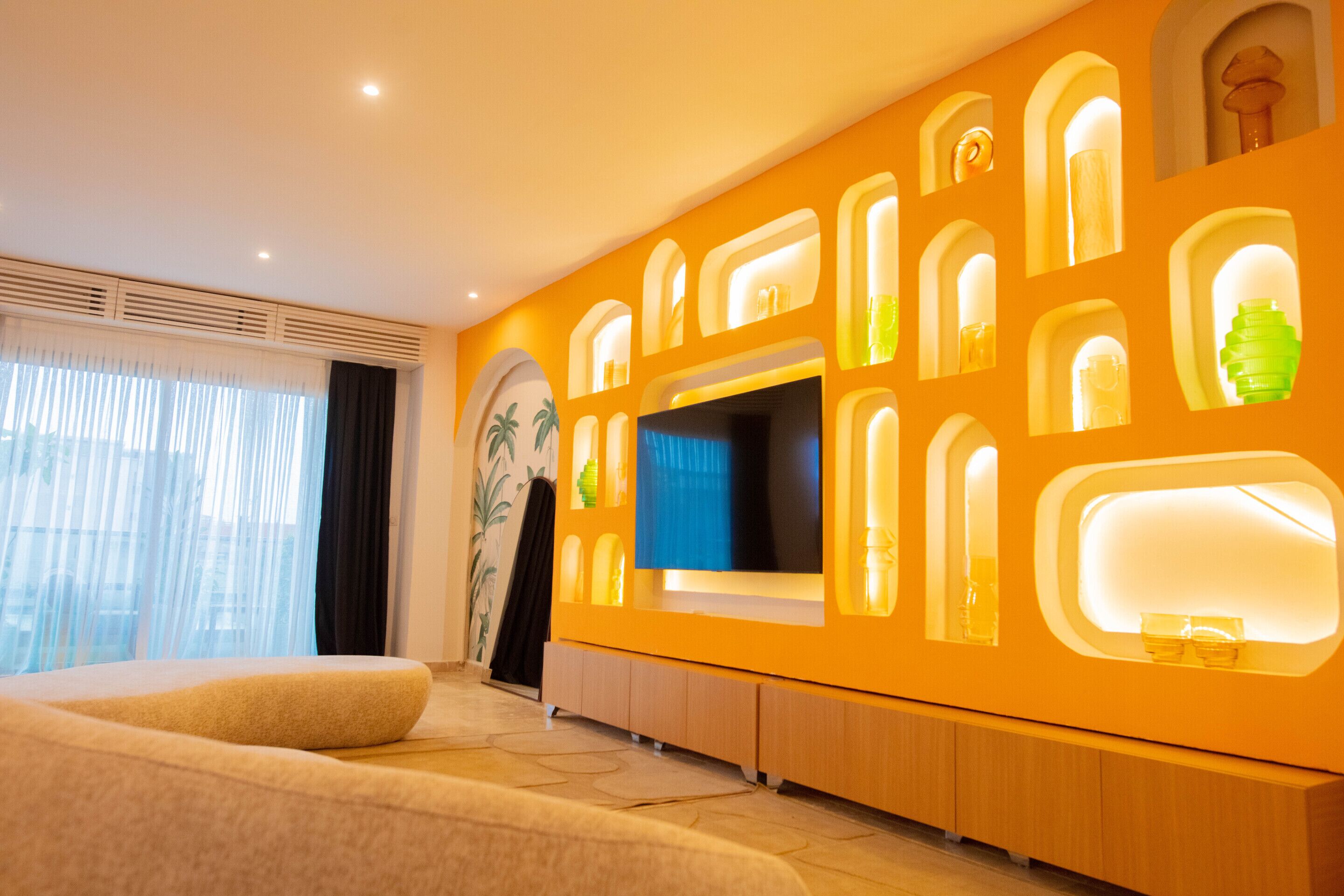 Een moderne hotelkamer met een groot bed, een flatscreen televisie en een wand met ingebouwde planken en verlichting.
