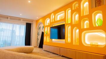 Een moderne hotelkamer met een groot bed, een flatscreen televisie en een wand met ingebouwde planken en verlichting.