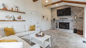 Una sala de estar con un sofá blanco, una mesa de centro, una chimenea y un televisor montado.