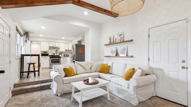 Una sala moderna con un sofá seccional blanco, una mesa de centro y una escalera que lleva a una cocina.