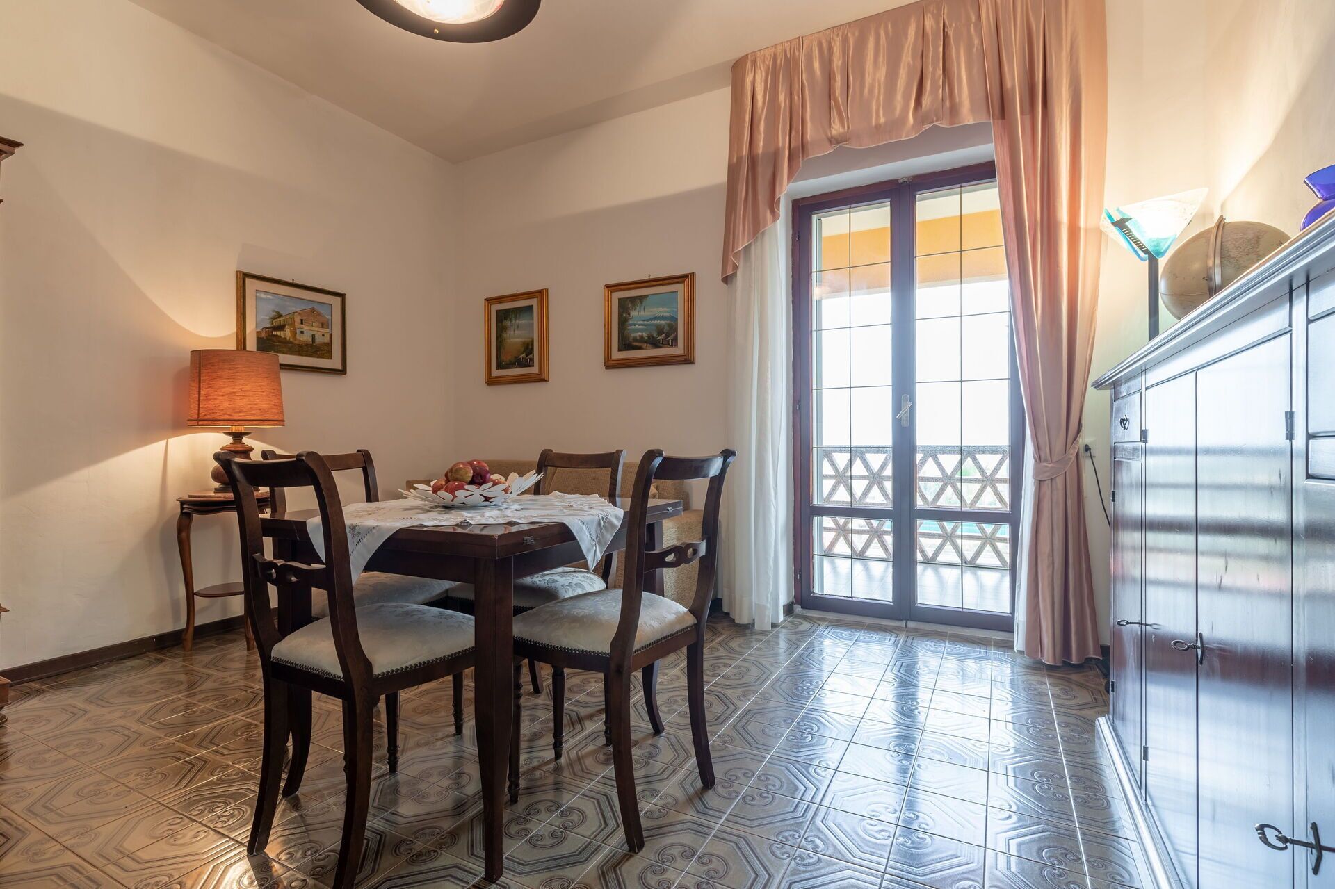 A dining area with a table set for four, four chairs, a lamp, and two framed pictures on the wall.