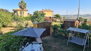 A patio with a table and chairs, surrounded by greenery and a view of houses in the background. - Italian Experience - Il Colle Sul Mare Holiday Home (Porto Recanati)