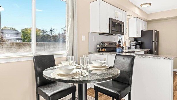 A modern kitchen with white cabinets, a black refrigerator, and a microwave. There is a dining area with a round table and black chairs. - Brand New! Lower Flat 1BR Near Downtown, Roseville (Roseville)