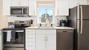 A modern kitchen with white cabinets, stainless steel appliances, and a window with a view of a residential area. - Brand New! Lower Flat 1BR Near Downtown, Roseville (Roseville)