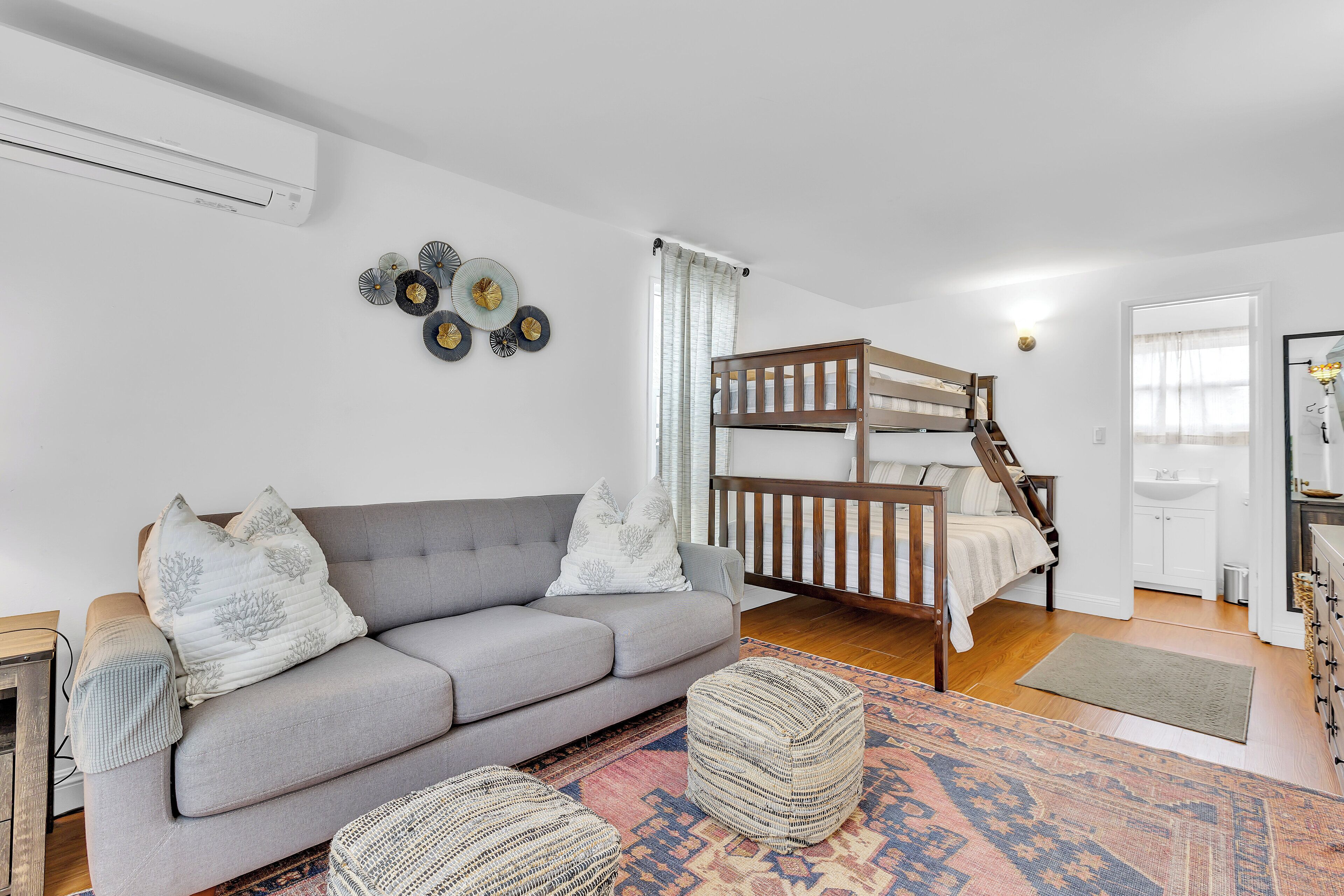 Una sala moderna con un sofá gris, una cama litera de madera y una alfombra estampada.