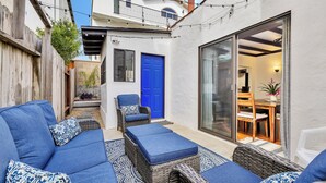 A patio area with a blue sofa, wicker ottoman, and chairs, a blue door, and a glass sliding door leading to an indoor dining area. - Historic "Spanish Jewel" at HOLLYWOOD BEACH (Oxnard)