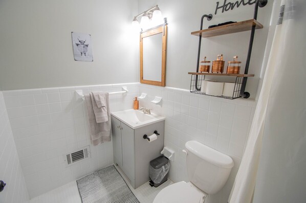 A bathroom with a white sink, toilet, and a mirror above the sink. There is a towel rack and a shelf with toiletries.