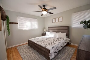 Ein Schlafzimmer mit Bett, Deckenventilator, Nachttisch, Lampe und Fenster mit Jalousien.