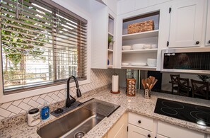 A kitchen with a stainless steel sink, a built-in stove, white cabinets, and a window with blinds.