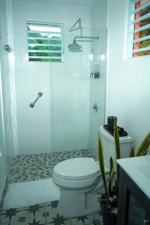Une salle de bain équipée de toilettes, d’une douche et d’une fenêtre donnant sur un espace verdoyant.
