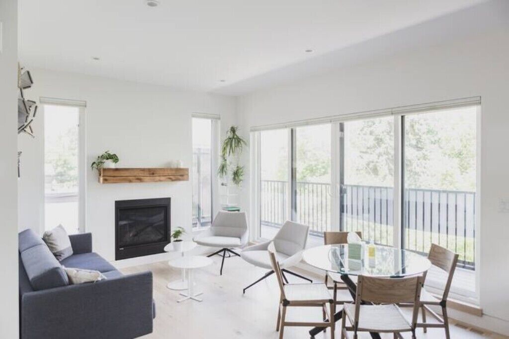 Una sala de estar moderna con chimenea, un comedor con mesa de vidrio y ventanas amplias que ofrecen vistas al exterior.