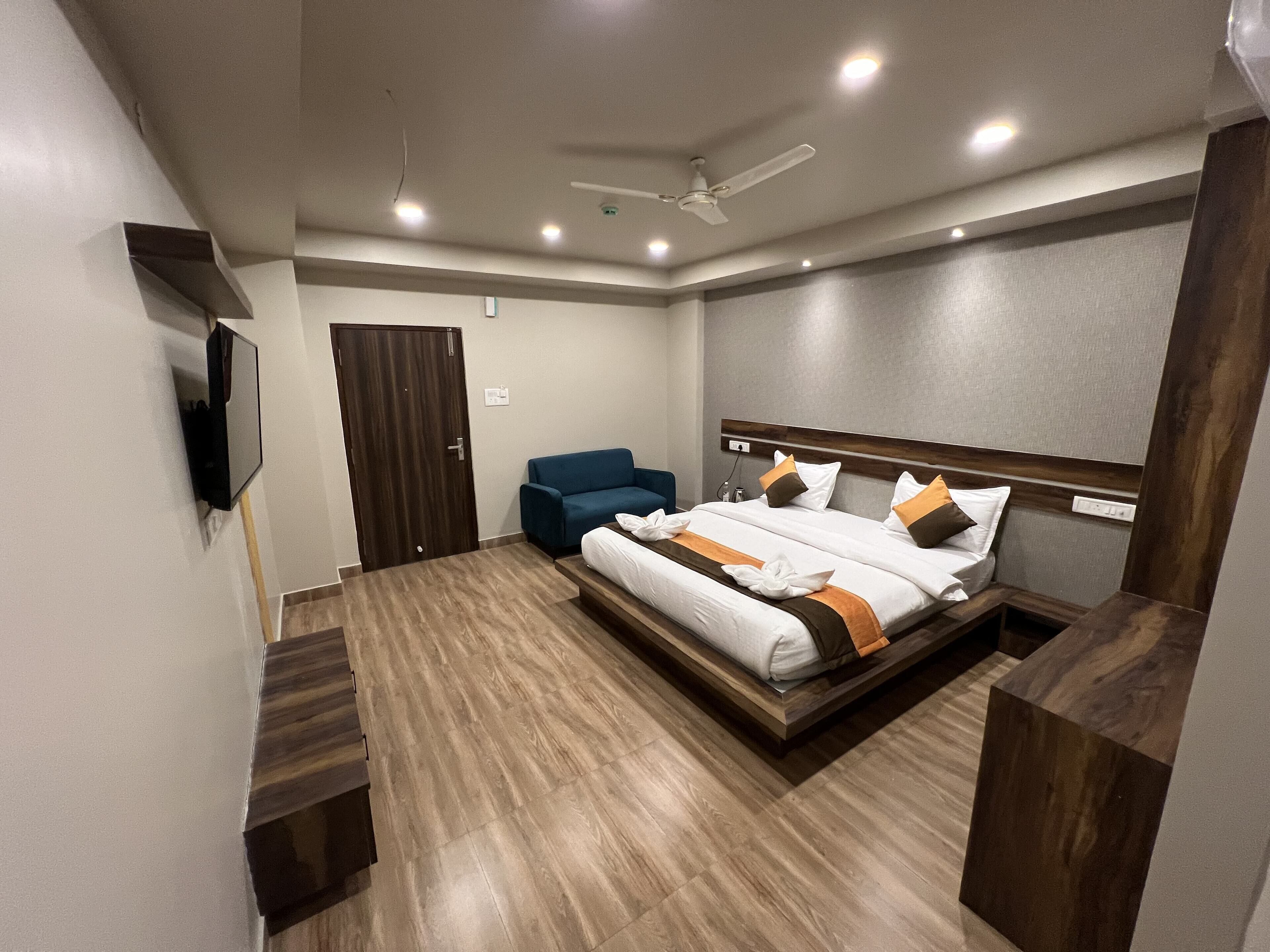 A modern bedroom with a bed, a blue chair, a ceiling fan, and a TV mounted on the wall.