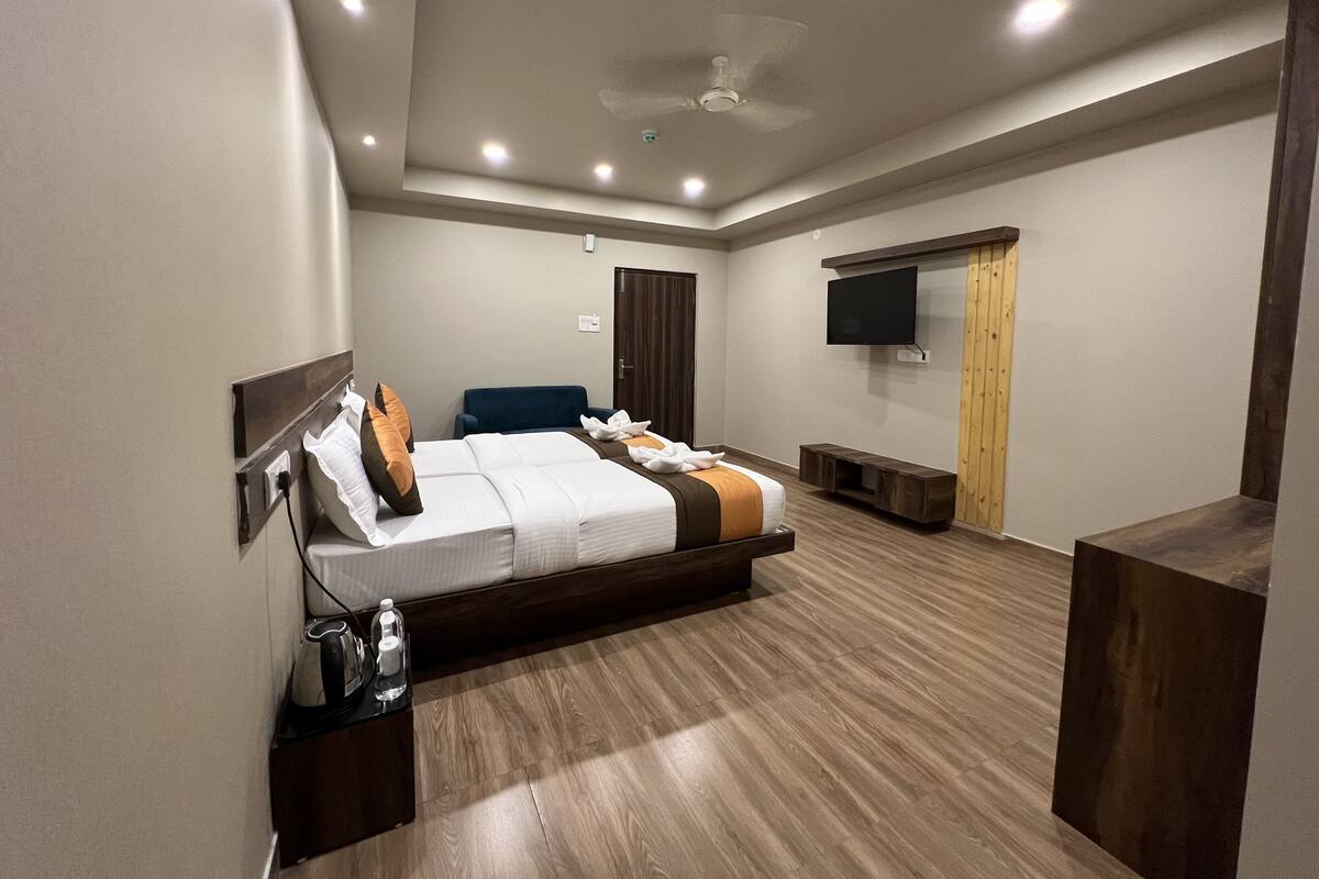 A modern hotel room with a large bed, a flat-screen TV, a ceiling fan, and a wooden floor.