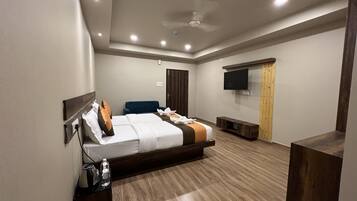 A modern hotel room with a large bed, a flat-screen TV, a ceiling fan, and a wooden floor.