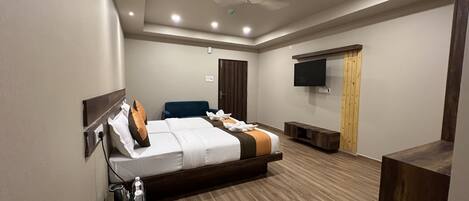 A modern hotel room with a large bed, a flat-screen TV, a ceiling fan, and a wooden floor.