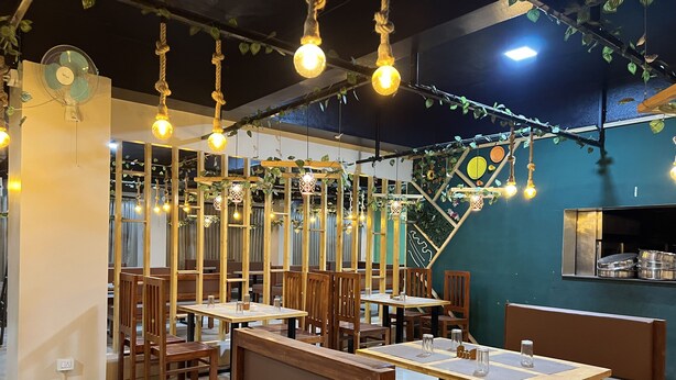 A restaurant with wooden furniture, hanging light bulbs, and a green accent wall.