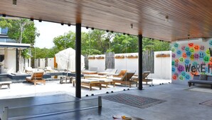 A covered outdoor area with lounge chairs, a pool, and a wall with a smiley face mural. - Nook Tulum by The Spot Rentals (Tulum)