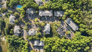 An aerial view of a residential area with multiple houses, a swimming pool, and a parking lot.