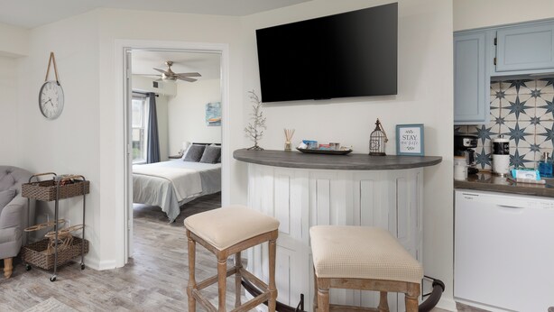 A modern kitchen with a flat-screen TV, a bar area with stools, and a dining table.