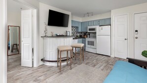 A modern kitchen with white cabinets, a flat-screen TV, and a bar area with stools.