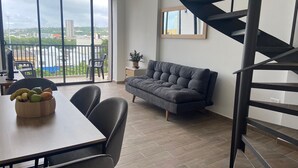 Una sala moderna con un sofá gris, una mesa de comedor con un frutero y una escalera en espiral.
