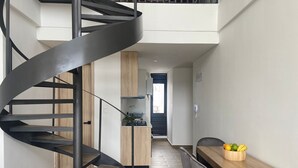 Una cocina moderna con una escalera en espiral, una zona de comedor con una mesa y sillas de madera, y vistas de la ciudad a través de un ventanal.