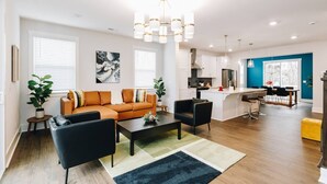 A modern living room with a sofa, coffee table, and chairs, a kitchen with white cabinets, and a dining area with a table and chairs. - Hot Tub • Game Room • Rooftop Fire Pit • Uptown (Charlotte)