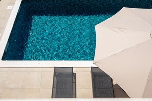 A swimming pool with clear blue water, surrounded by tiled flooring and two lounge chairs with a beige umbrella. - Wunderschöne Villa mit Schwimmbad, Grill, Wifi, Kostenloses Wlan (Dračevac)