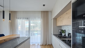 Eine moderne Küche mit Holzarbeitsplatte, Edelstahlgeräten und einem großen Fenster mit transparenten Vorhängen.