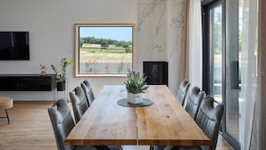 Ein Essbereich mit Holztisch und Stühlen, einer Topfpflanze und einem großen Fenster mit Blick auf ein Feld.