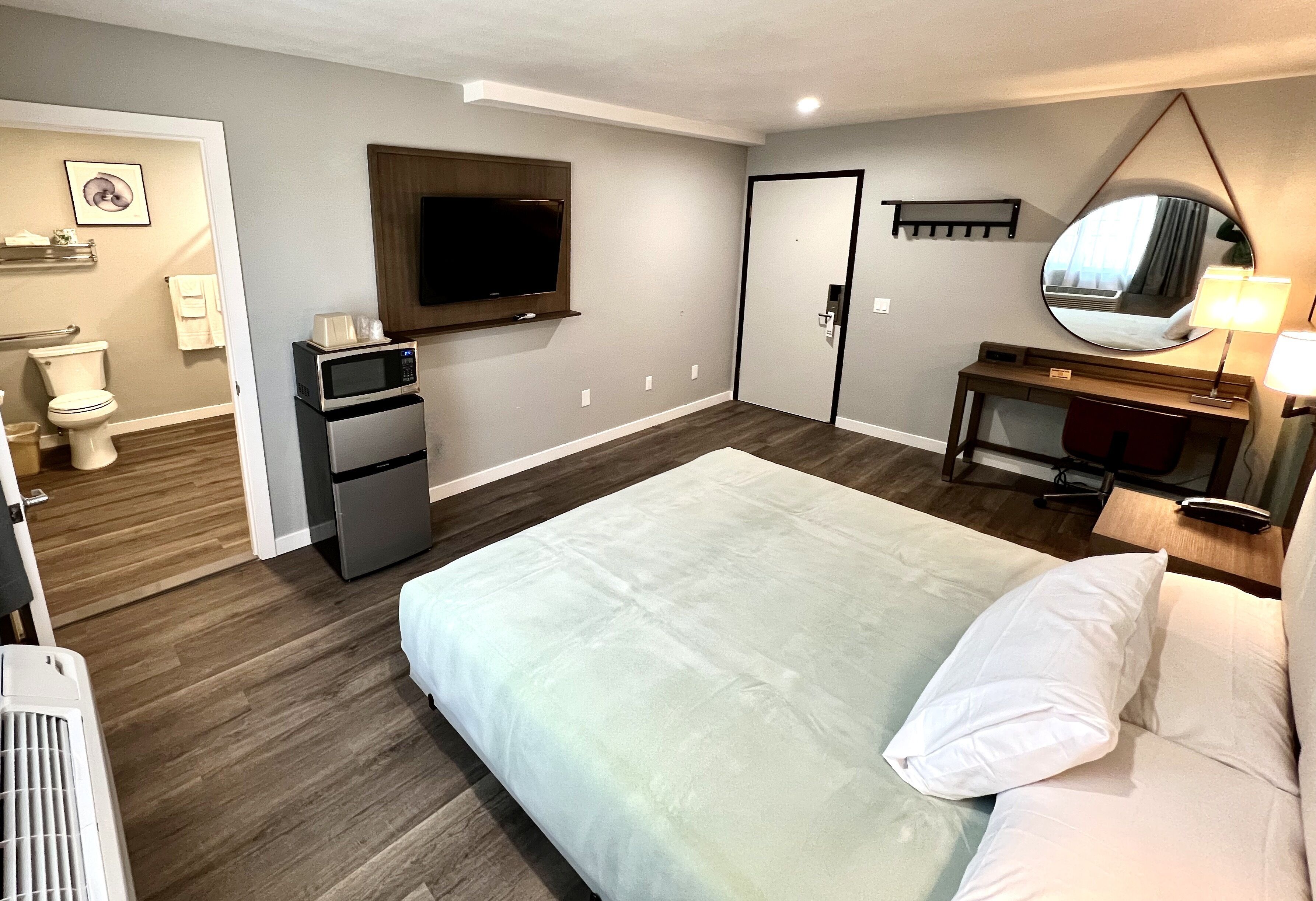 Una habitación de hotel con cama, escritorio, televisor, microondas y puerta.