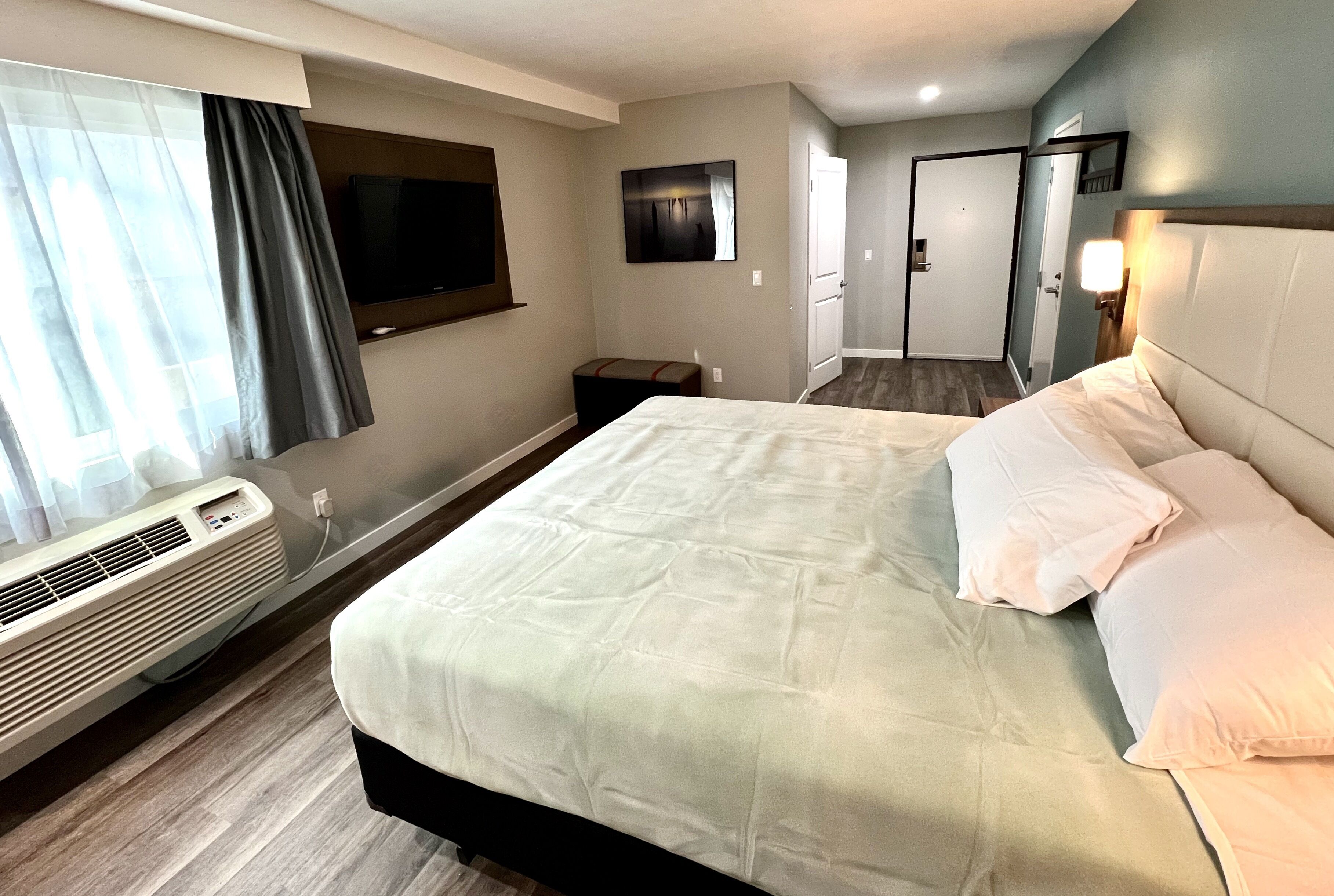 A hotel room with a large bed, a flat-screen TV mounted on the wall, a heater, and a door leading to another room.