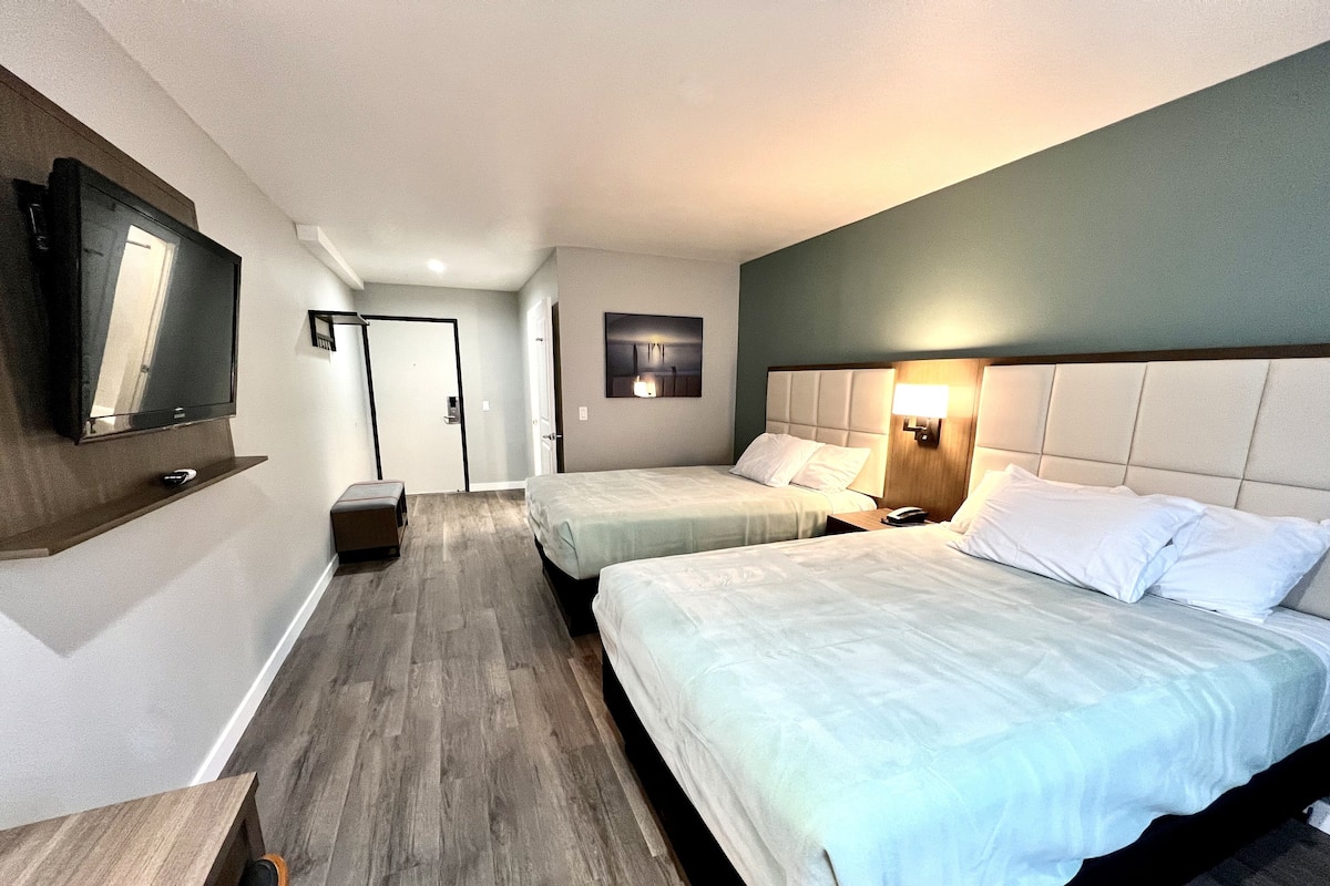 Quarto de hotel com duas camas, televisão, escrivaninha e porta para o banheiro.