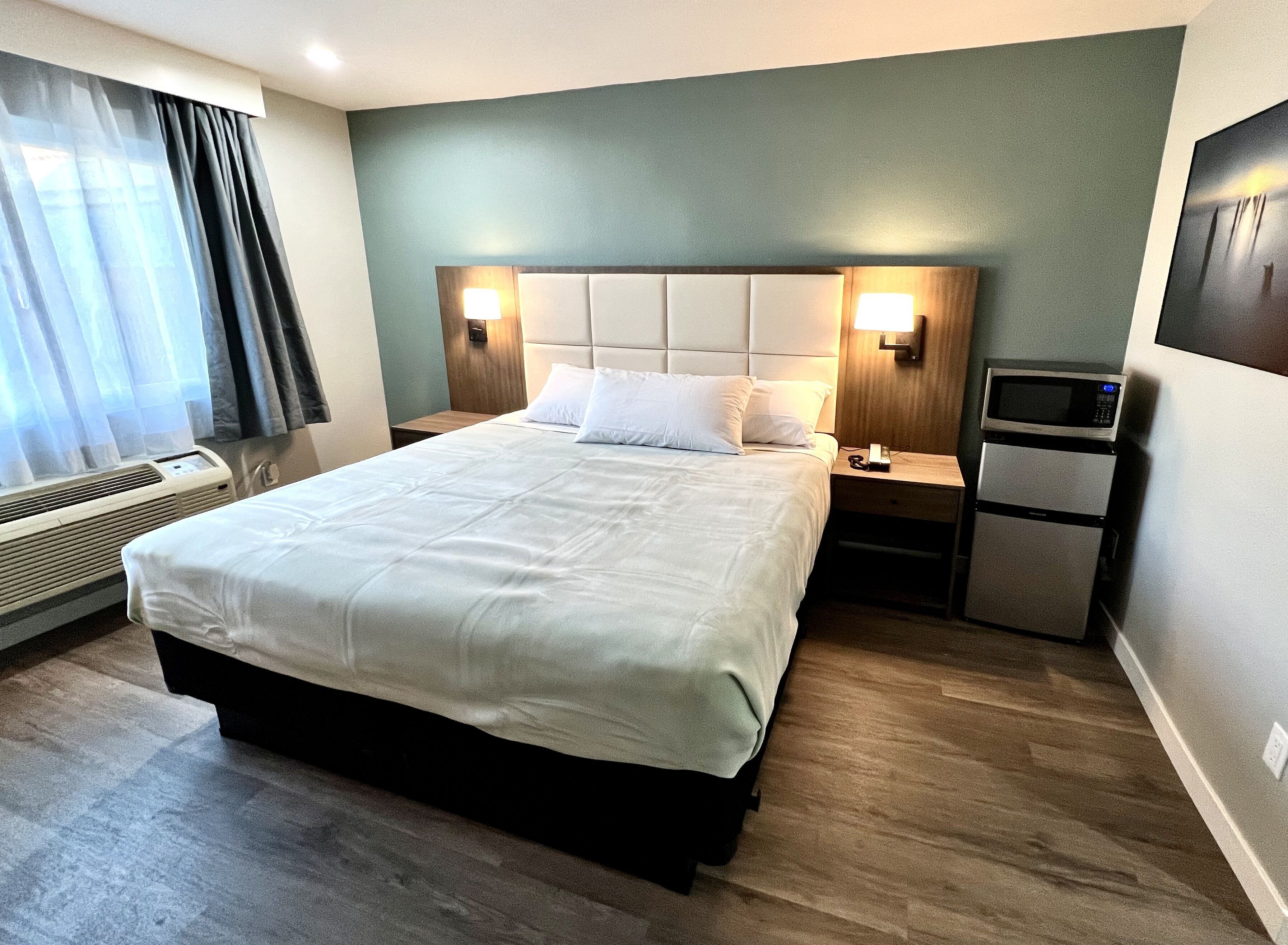 Une chambre d’hôtel dotée d’un grand lit, de deux tables de chevet, d’un téléviseur fixé au mur et d’un système de climatisation intégré.