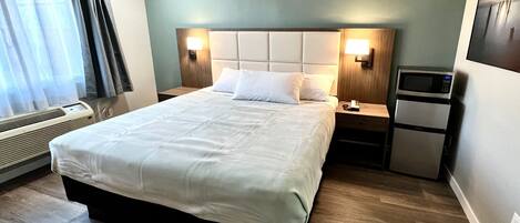 A hotel room with a large bed, two bedside tables, a wall-mounted TV, and a built-in air conditioning unit.