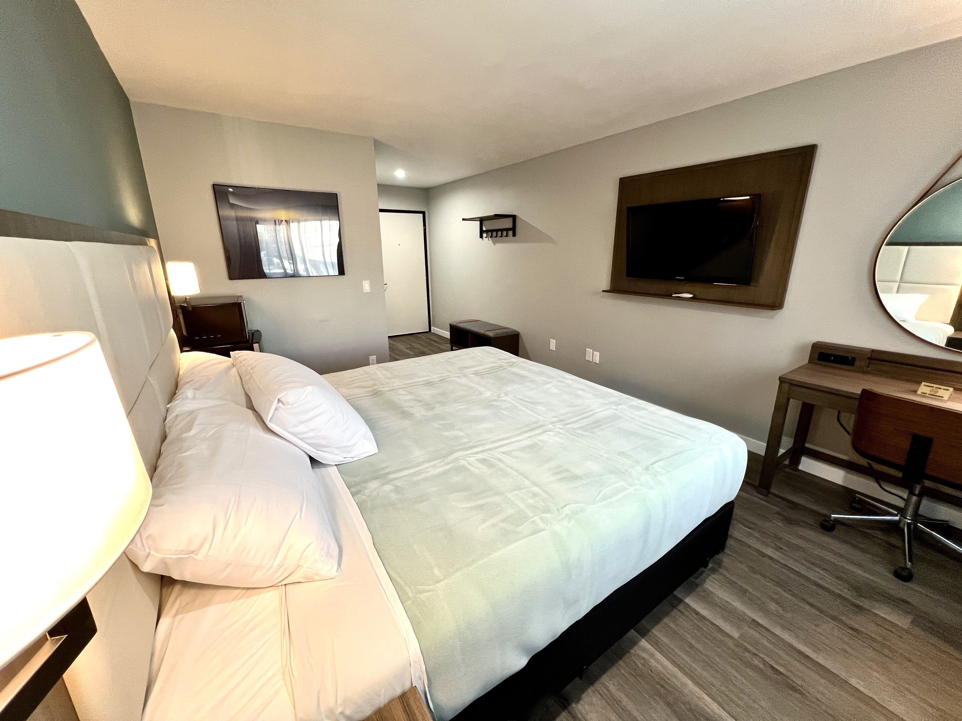 Hotellihuone, jossa on suuri sänky, työpöytä, tuoli, televisio ja peili.