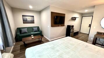 Een hotelkamer met een bed, een groene bank, een salontafel, een televisie, een magnetron en een klein bureau.