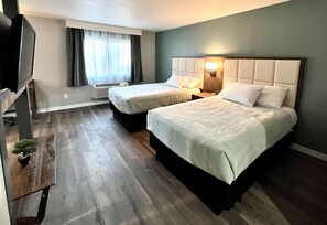 A hotel room with two beds, a TV, a small table with a plant, and a window with curtains.